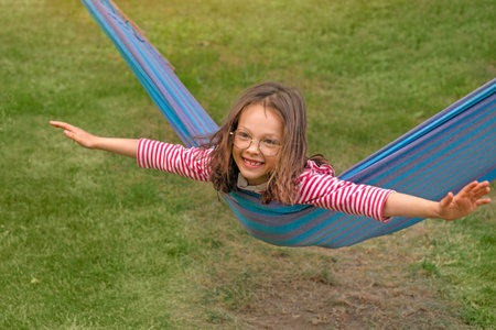 A child lies across a hammock, swinging with outstretched arms, depicting an airplaneの写真素材