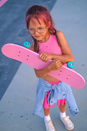 A stylish girl stands with a skateboard in hands in a skate park. Active sports hobbies