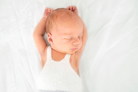 A cute newborn baby in bed sleeps with his arms raised to the top. Healthy cute infant