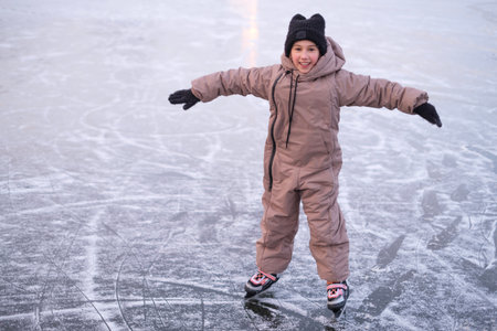 A child learns to skate on the ice rink of a frozen lake while keeping his balance.