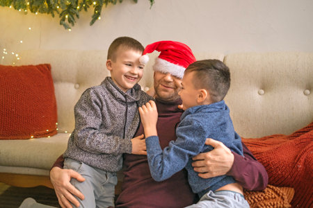 Boys hug their father in a New Year's red hat. The family is having fun on Christmas Eve.