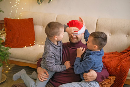 The sons put a Santa Claus hat on their dad. Father has fun with children on the eve of New year and Christmasの写真素材