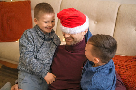 A father in a red Santa Claus hat plays with children.の写真素材