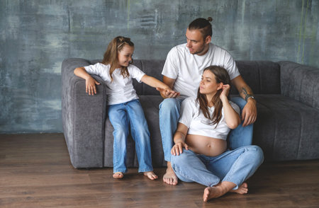 A pregnant mother is sitting on the floor next to her husband and young daughter. The family is waiting for the birth of their second baby.のeditorial素材