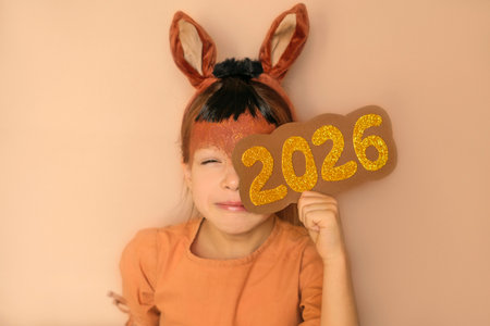 A narrowed, sly girl looks out with interest from behind the numbers 2026.の写真素材