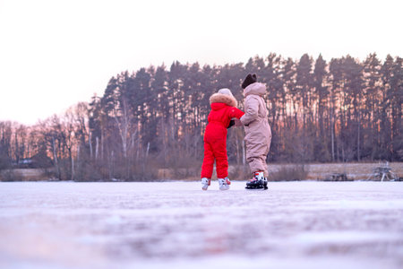 The girl supports her sister by the arms, keeping her from falling while skating. Outdoor Ice Skating Rinkの写真素材