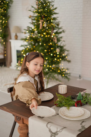 The girl helps the family to arrange the plates on the festive table on Christmas Eve. Preparing for the New Year celebrationの写真素材
