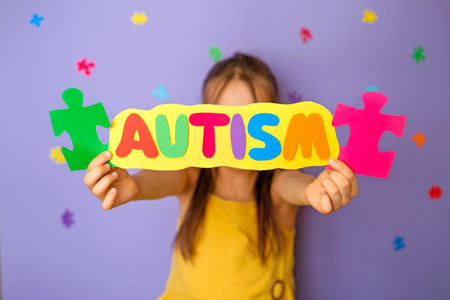 A faceless child shows a cardboard postcard with the word autism, made up of colorful letters of different colors. Support and awareness for people with autism spectrum disorderの写真素材