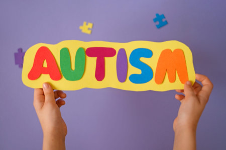 Colorful paper letters spelling autism in child hands. Autism awareness, inclusive education, social support, early learning and childhood development concept.の写真素材