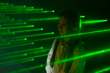 A girl in the green rays of a maze laser in a black room of a children's entertainment center.の写真素材