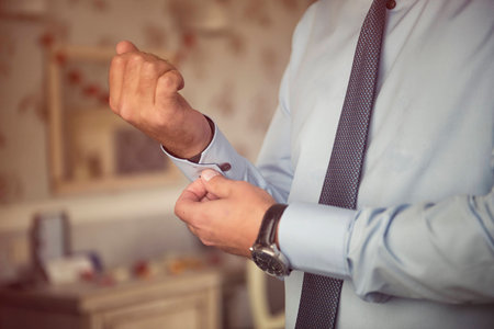 Male hands fixing stylish silver cufflinks on blue shirt cuffs sleeves in formal suitの写真素材
