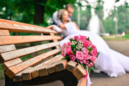bouquet on wooden bench with bride and groom in the background, focus on the flowersの写真素材
