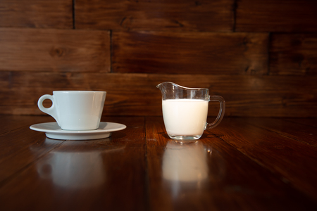 milk in glass milk jug with white cup and reflection from a wooden tableの写真素材