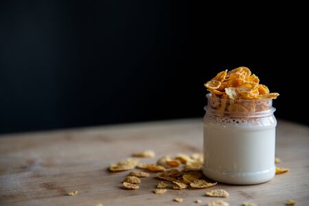 jar of yogurt with cornflakes stands on a wooden board and black background with copy spaceの写真素材