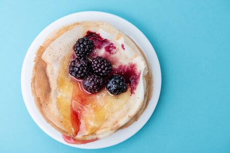 Stack of thin pancakes poured with honey and decorated with fresh strawberries and blueberries side view with selective focus and light background with copy spaceの写真素材