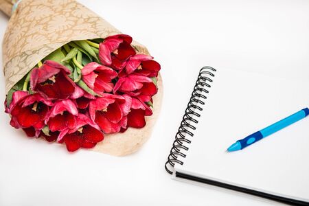 Flat lay of red bouquet tulips isolated on white with notebook and pen with empty place for your textの写真素材
