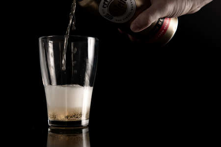 VOLGOGRAD, RUSSIA - APRIL 25, 2020 : Male hand pours beer into a glass from Aluminium can of Warsteiner Beer on black background with copy space. Product of Germanys largest privately owned brewery.のeditorial素材