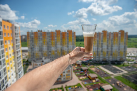 a glass of coffee on a mans hand stretched out into the window against the background of an apartment buildingの写真素材