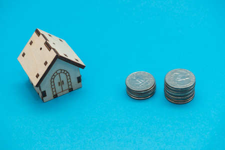 Model toy house and us coins stack on blue background. Mortgage and real estate concept.の写真素材