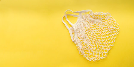 Reusable cotton shopping string bag on bright yellow background. Copy space. zero waste concept, no...