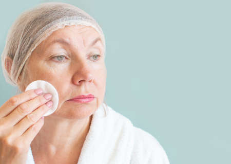Portrait of a sad woman seniora with a cotton pad. Natural spa treatments at home, body care concept, organic cosmetics. Anti aging, cosmetology, fatigue, thinking old age and illness, pensionerの写真素材