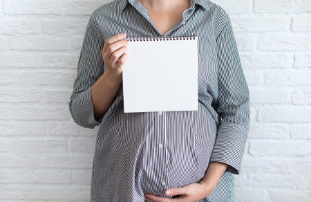 Mockup white sheet pregnant woman in office dress, holding blank white card near belly, place for text. Wish list before childbirth, shopping list, planning shopping. Copyspaceの写真素材
