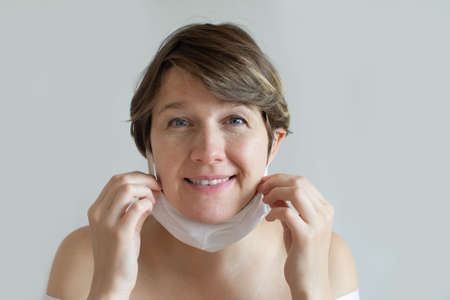 Portrait young cheerful woman taking off her cotton linen mask. Pandemic thinking concept, health.の写真素材