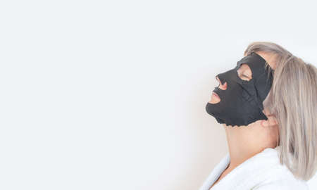 Senior woman profile, applies a black cosmetic mask to her face. Anti age concept. Mature woman face after spa treatment. Beauty spa treatment. Place for textの写真素材