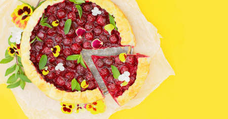 Spring cherry pie, decorated with edible flowers on a yellow background. Hello summer. Concept baking, cookbook recipes, bakery banner, cafe advertisement. Vacation sales spring, summer and holiday.の写真素材