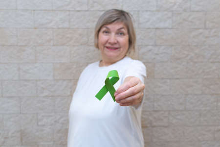 Woman holds a sign with a green ribbon for awareness and support of people living with disease. Awareness of liver cancer, kidney cancer, gallbladder cancer and lymphoma. Mental, Psychosocial supportの写真素材