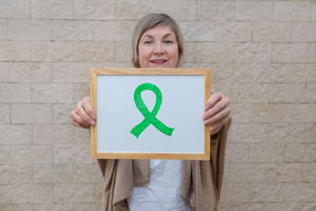 Woman holds a sign with a green ribbon for awareness and support of people living with disease. Mental, Psychosocial support. Awareness of liver cancer, kidney cancer, gallbladder cancer and lymphoma.の写真素材