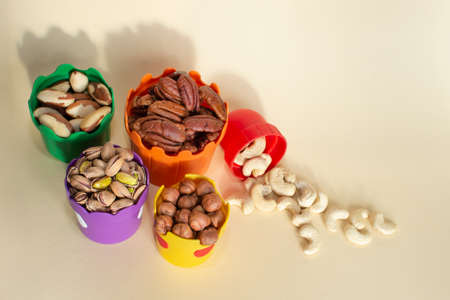 Nuts for children in colorful cups. Walnuts, pistachio, hazelnuts, brazil nuts, cashews, pecans. Useful snack. Healthy food, useful microelements and vitamins, healthy eating. Selective Focusの写真素材