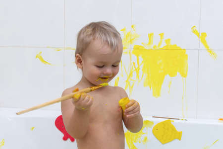 Kid draw with paints in the bath, playing at home. Todler draw with educational toys for creativity. Boy play at home. Bright paint gouache stained face and hands of a child.の写真素材