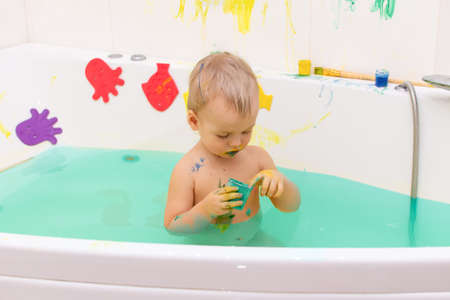 Kid draw with paints in the bath, playing at home. Todler draw with educational toys for creativity. Boy play at home. Bright paint gouache stained face and hands of a child.の写真素材