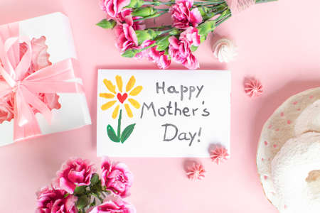 Mother day greeting card on pink background. Breakfast, carnation gift and a postcard made by the child for mom.の写真素材