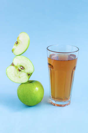 Apple juice levitation. Balance of fresh green apple slices and a glass of apple juice on a blue background. Balance food levitate conceptual creative still life. Levitation food balance symbolの写真素材