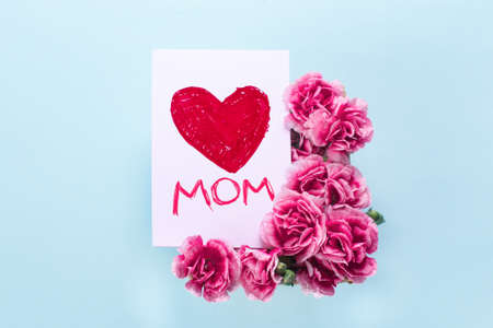 Mother day card on blue background. Text LOVE heart mom. Carnation and a postcard made by the child...