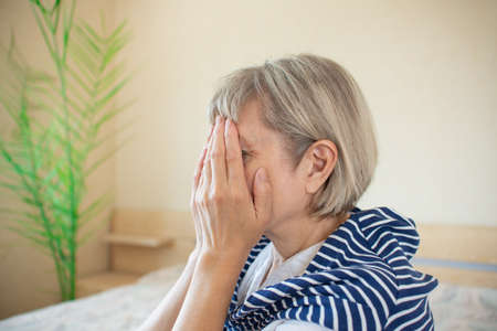 Senior woman addict and alcoholism alone depression stress sitting on the bed with her head in her hands. headache dizziness, migraine. Social documentary conceptsの写真素材