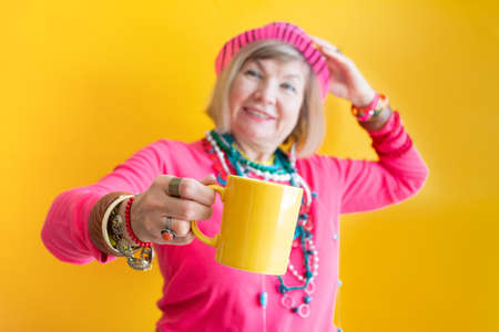Happy Senior woman funny face drinking a cup of coffee or tea in stylish clothes. Concepts senior people on colored backgroundの写真素材