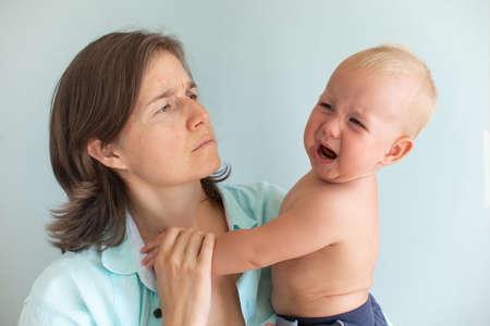 Tired mom trying to calm her crying infant baby on hands. Newborn tantrum. Motherhood concept....