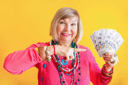 Happy elderly woman with a cashback money bundles in stylish clothes on a yellow background. Finances and people conceptの写真素材