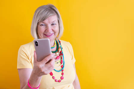 Happy mature elderly senior lady woman talking mobile cell phone in stylish clothes on yellow backgroundの写真素材