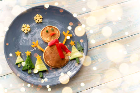 Christmas pancake healthy shaped like a snowman with fresh vegetables blue plate on wooden white table decorated festively. Christmas fun food for kids, funny breakfast brunch idea xmasの写真素材