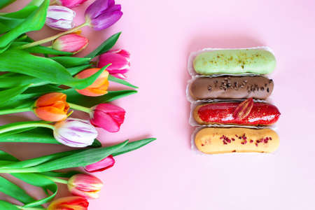 Eclair is a traditional French pastry and colorful tulips flower composition over pink background ....