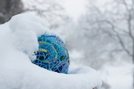 Cold snow day with close-up with shades of blue, aqua, green, gold, bright multicolored stained glass mosaic garden art ball in winterの写真素材