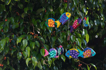 Colorful cheerful painted fish mobile hanging in a tree with red berries, spring and summer fun.の写真素材