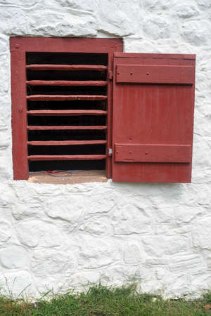 Red slatted window and shutter on whitewashed colonial stone wall.