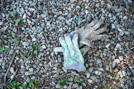 Workgloves on a gravel drive, stone area. Gloves are heavily worn and have a flower pattern on them. Shot in natural light, off center placement for copy space, and no people.の写真素材
