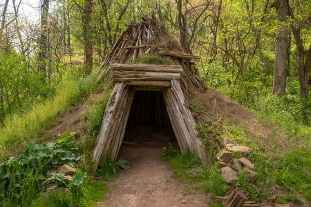 Collier's hut one-person shelter made out of wooden poles and mud sod exterior. Enchanted shaman sweat lodge concept in idyllic nature background. Beautiful nature setting with long shadows for magical feeling.の写真素材