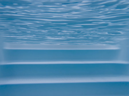 Tranquil and serene image of white pool steps seen underweater with rippling water surface above and blue pool liner below. Clean relaxing water and sunlight. No people, with copy space.の写真素材